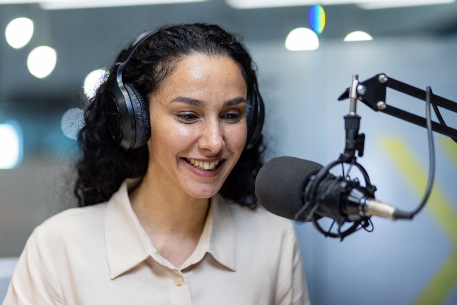 Smiling woman recording podcast in studio with headphones and microphone